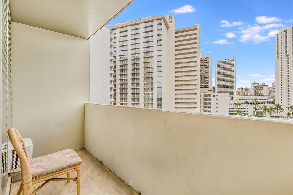 A private urban balcony overlooks high-rise buildings and palm trees scattered throughout the vibrant cityscape under a clear blue sky.