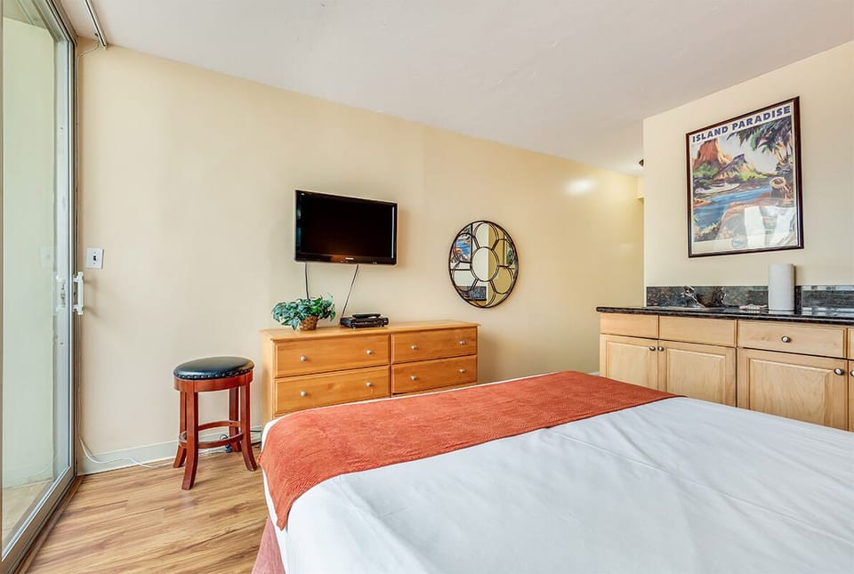 Your cozy bedroom features a comfortable bed, flat-screen TV, and tropical artwork that sets a relaxing island vibe for your getaway.