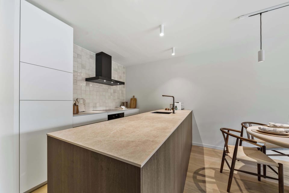 Designer kitchen with central island, bar seating and premium appliances flowing into the dining space in this luxury 2-bedroom apartment in De Haan, perfect for self-catering family holidays near the North Sea beach.