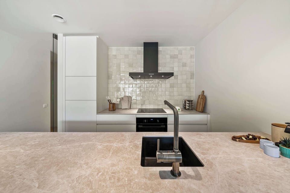 Modern open kitchen with induction hob, sleek cabinetry and a stylish tiled backsplash in this luxury De Haan holiday apartment, fully equipped for easy self-catering near the North Sea beach and Belgian coast.