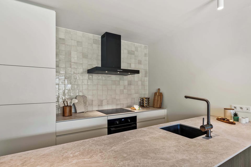 Contemporary kitchen with induction cooktop, a classic tiled backsplash and ample worktop in this luxury De Haan apartment, with everything you need for self-catering holidays by the North Sea and beach.
