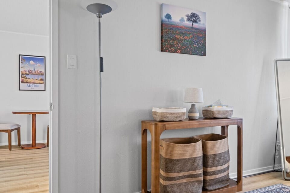 A welcoming entryway features a wooden console table, woven baskets for storage, and local Austin artwork to set the tone for your stay.