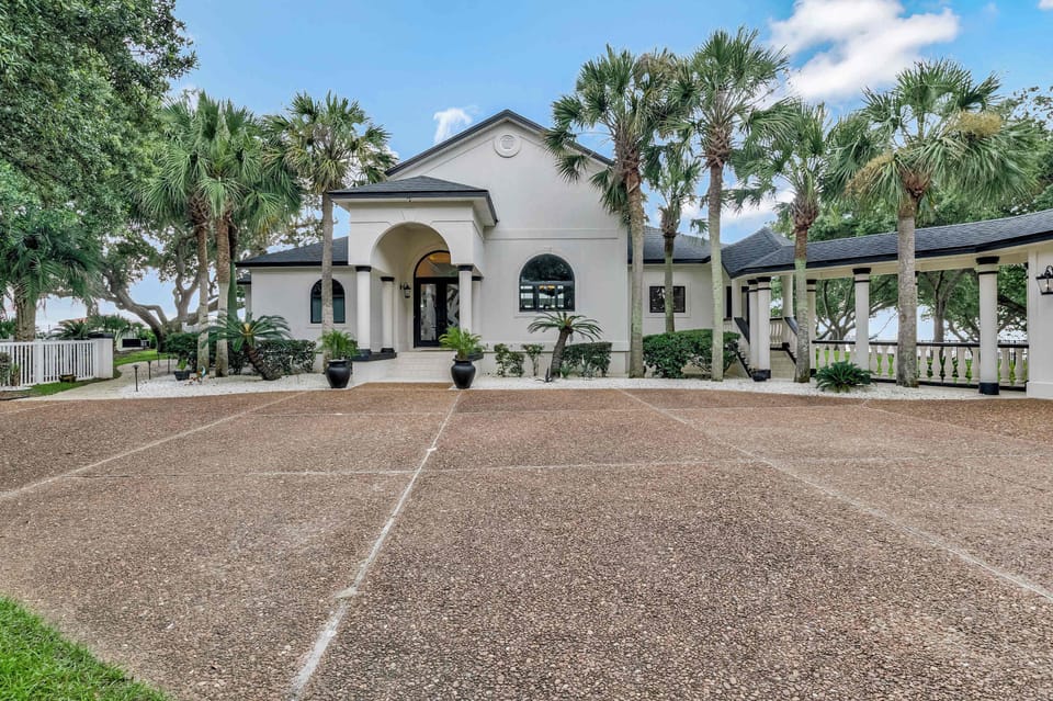 Mediterranean-style architecture, an arched entryway, and swaying palm trees define the exterior of this Perdido Key vacation home. A wide paver driveway offers ample parking for multiple vehicles.

