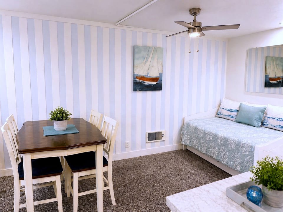 Coastal-chic studio with dining for four, daybed, and ceiling fan comfort.