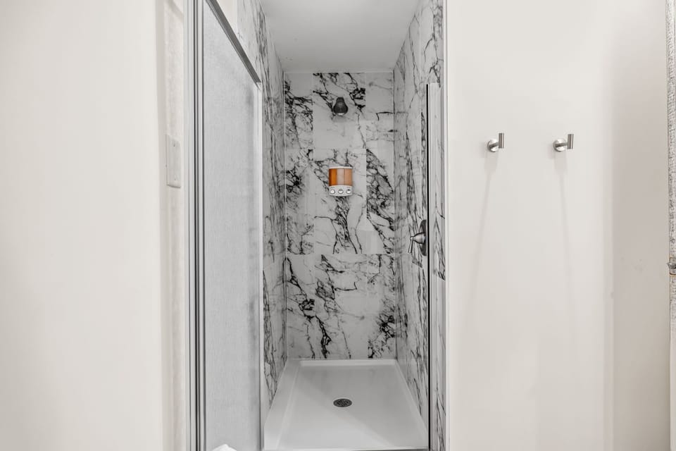 Walk-in shower with marble-look walls and wall-mounted toiletries.