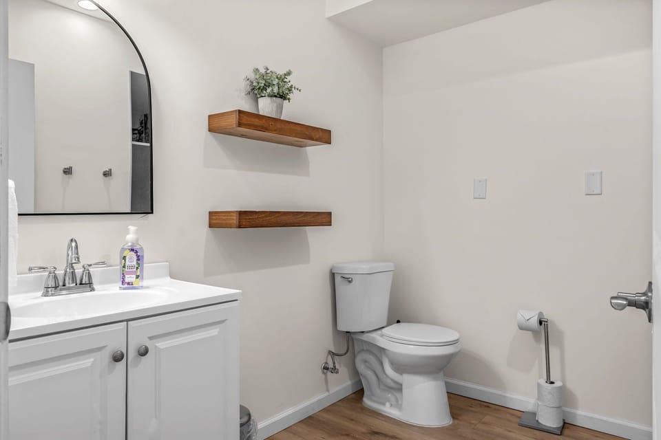 Bathroom with a white vanity, arched mirror, toilet and wood floating shelves.