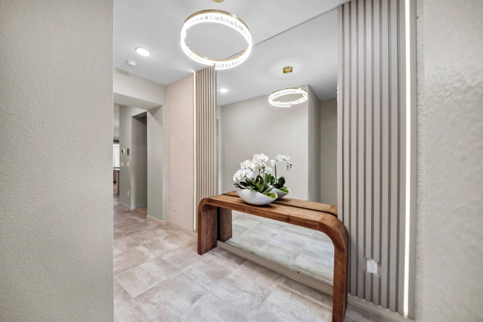 Enter a bright, inviting space with soft neutral tones and sleek finishes, accented by modern light fixtures and a stylish wooden console table. An elegant mirror enhances the welcoming atmosphere, complemented by fresh flowers.