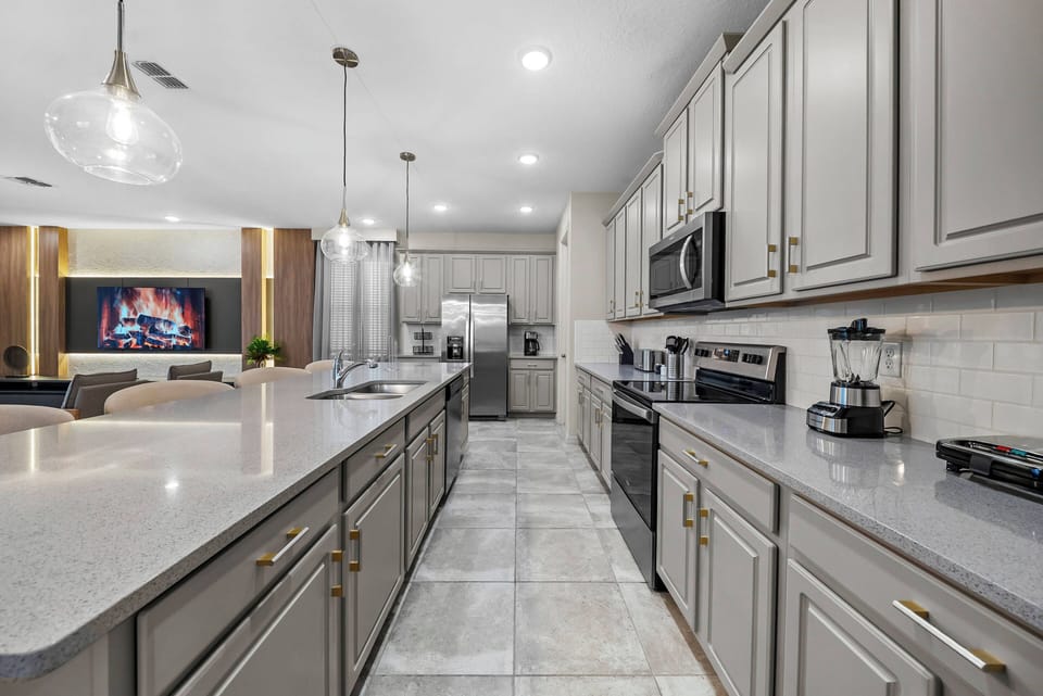Enjoy a stylish kitchen featuring sleek gray cabinetry and spacious light countertops, ideal for culinary creativity. The warm pendant lighting and modern appliances set a welcoming mood for cooking and gatherings.