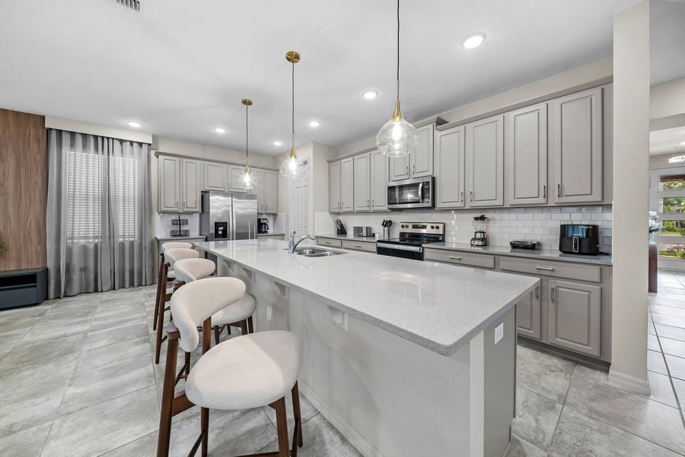 Enjoy a beautiful kitchen with elegant gray cabinetry and light marble countertops, perfect for a fresh atmosphere. The spacious island with stylish bar stools is great for casual gatherings, enhanced by warm pendant lighting for.