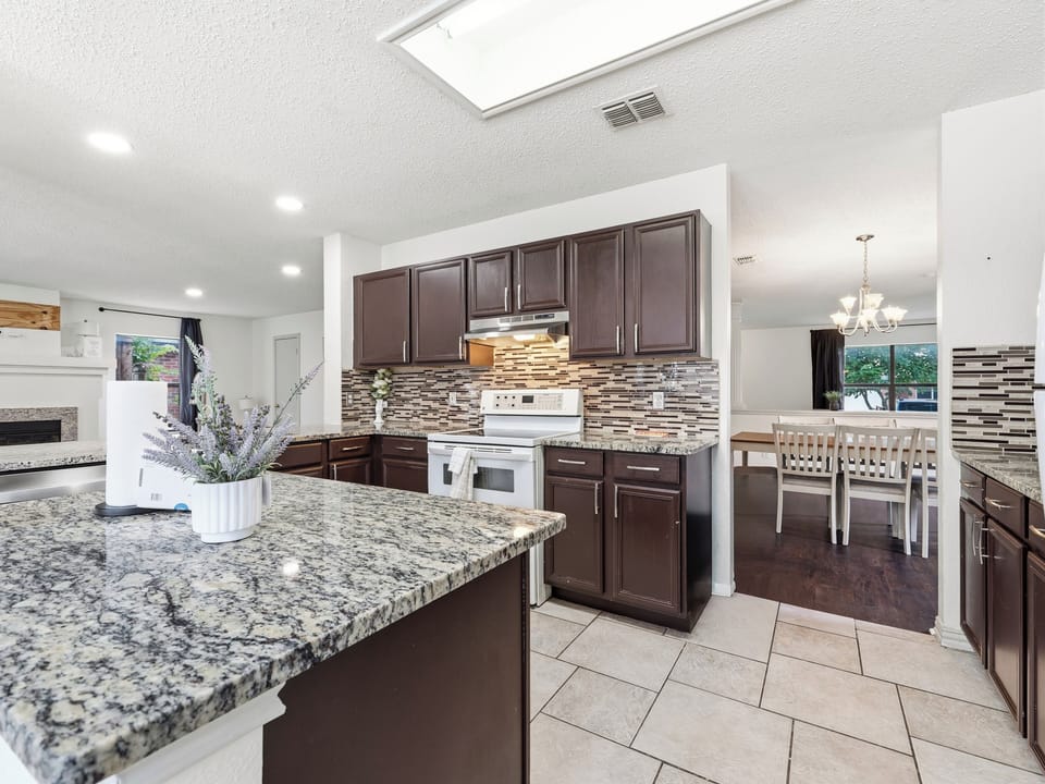 Prepare your favorite meals in this spacious, fully equipped kitchen with granite countertops, elegant backsplash, and modern appliances—flowing seamlessly into the bright dining area where you'll share meals together.