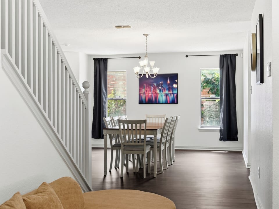 Picture yourself gathering around this welcoming dining table, where natural light pours through dual windows and a charming chandelier sets the perfect ambiance for your morning coffee or evening meals together.