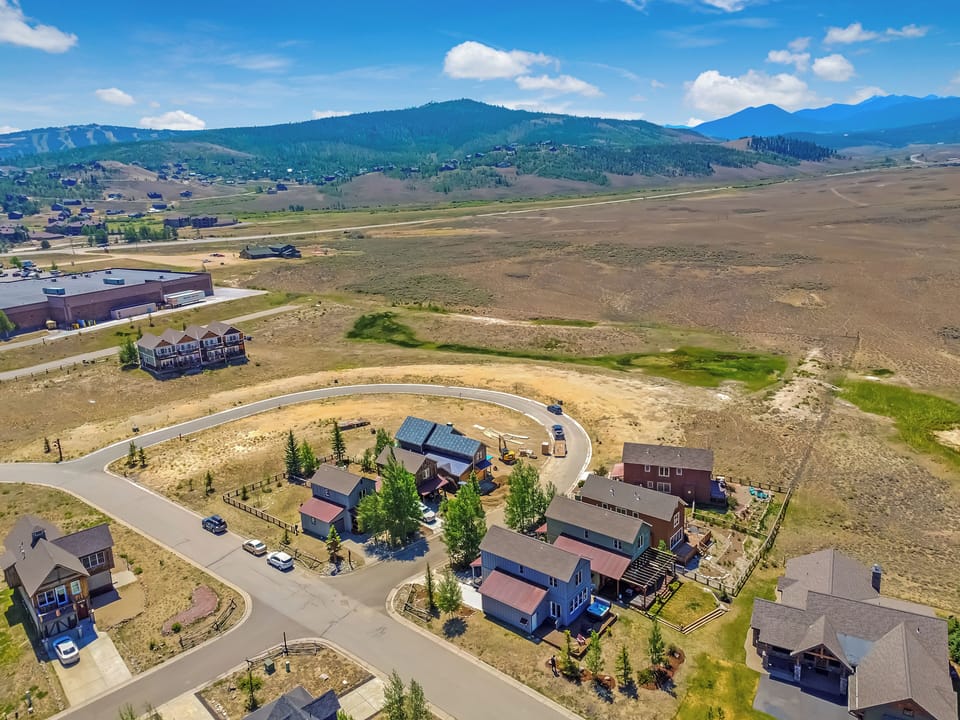 Aerial view of vacation rental properties nestled in a scenic mountain valley with sweeping panoramic views of forested peaks and open terrain.