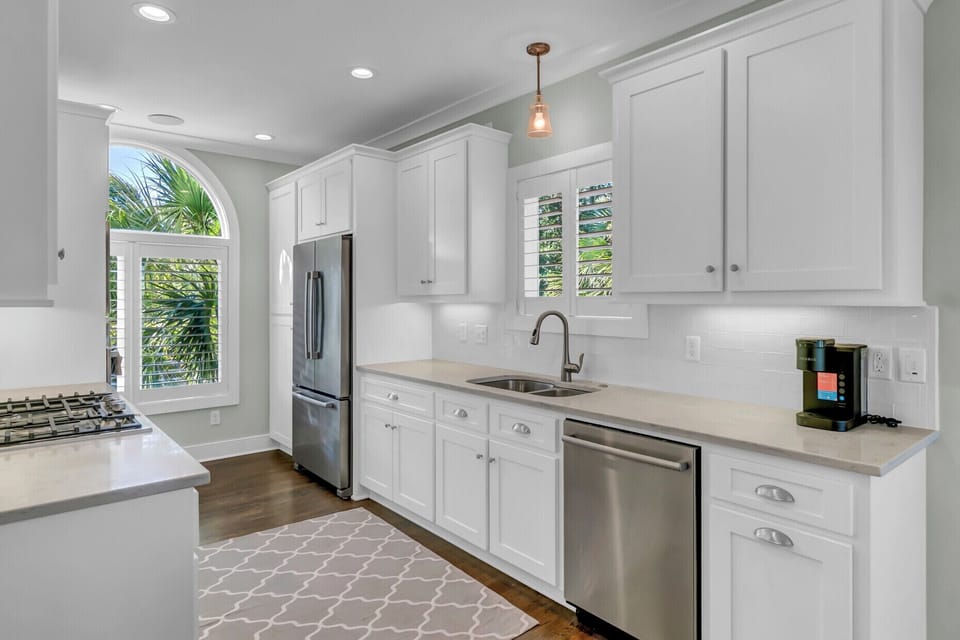 Step into your bright, fully equipped kitchen featuring stainless steel appliances, elegant white cabinetry, and a charming arched window framing lush palm views—perfect for preparing meals in style.