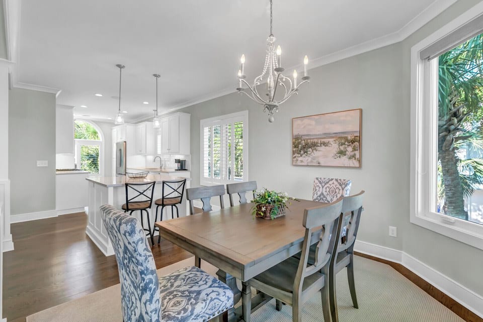 Picture yourself sharing meals at this elegant dining table, bathed in natural light from large windows, while an open kitchen invites easy conversation. The chandelier adds a touch of charm, making every gathering feel special.