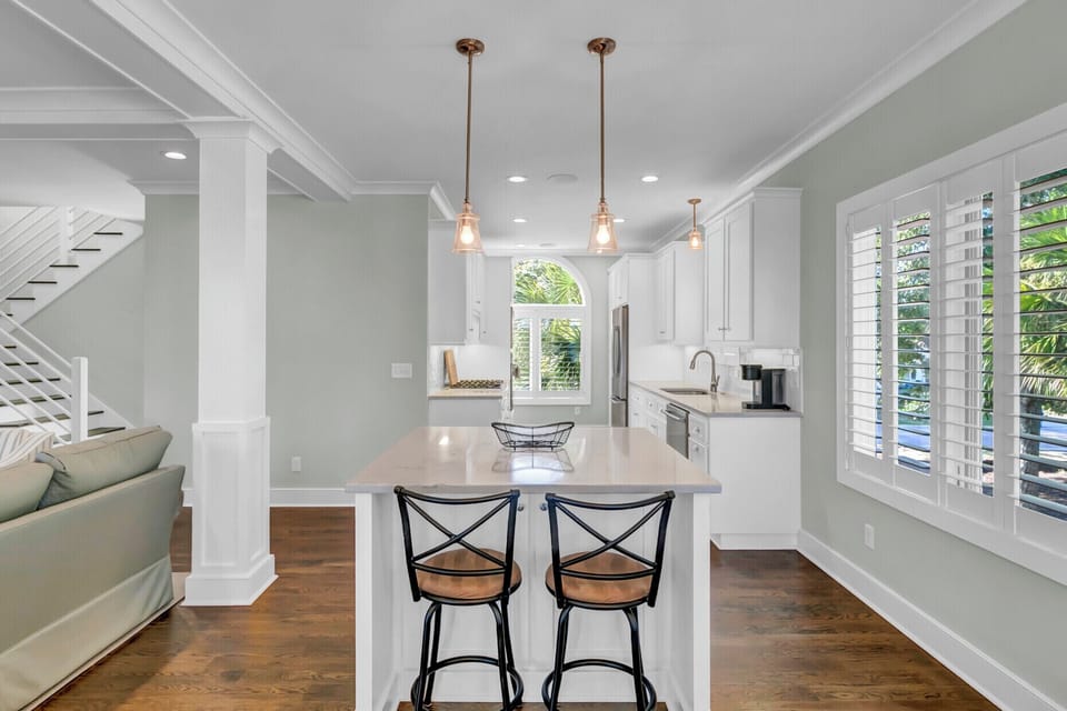 Gather at your sunlit kitchen island where coastal charm meets modern comfort. White cabinetry and gleaming countertops make meal prep a breeze while natural light streams through plantation shutters.