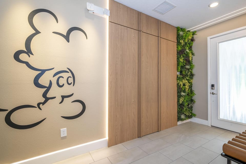 Light gray tiled entry features wood panel closets, frosted glass door with keypad lock, and a vertical green plant wall.