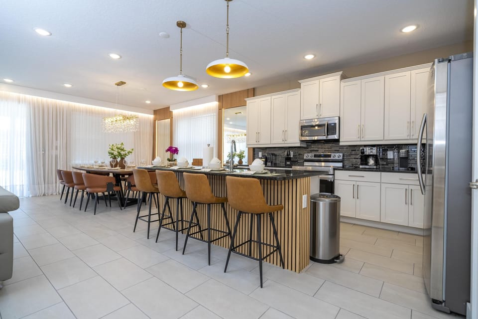 Kitchen with white cabinetry, black tiled backsplash, stainless steel appliances, and a large island with brown leather barstools.