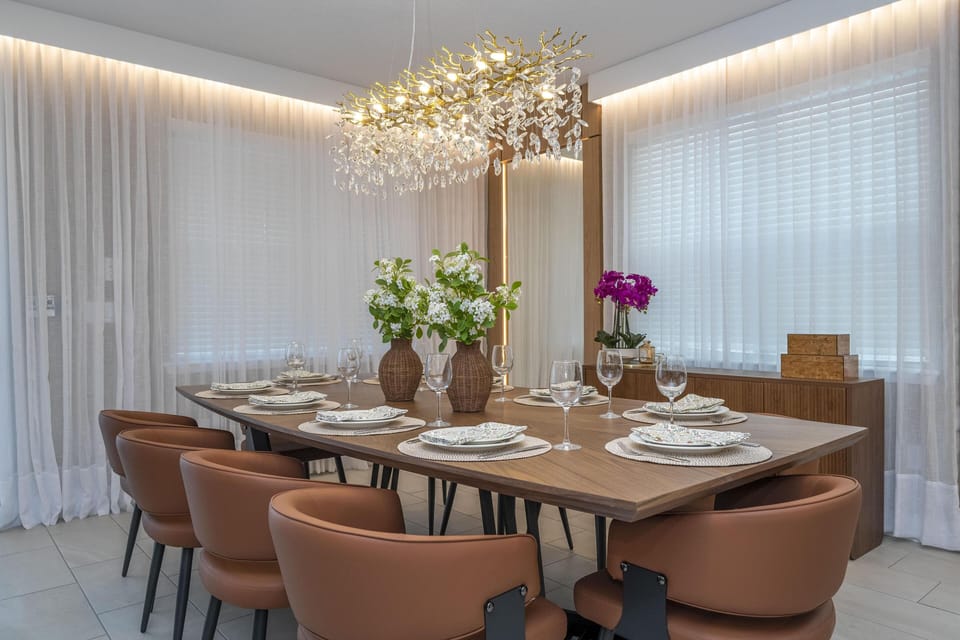 Rectangular wood dining table set with eight brown leather chairs under a gold and crystal chandelier.