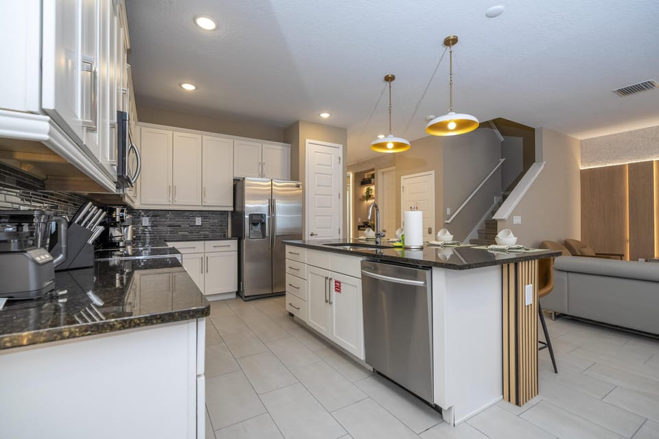 Kitchen with white cabinetry, black granite countertops, stainless steel appliances, and two pendant lights over the island.