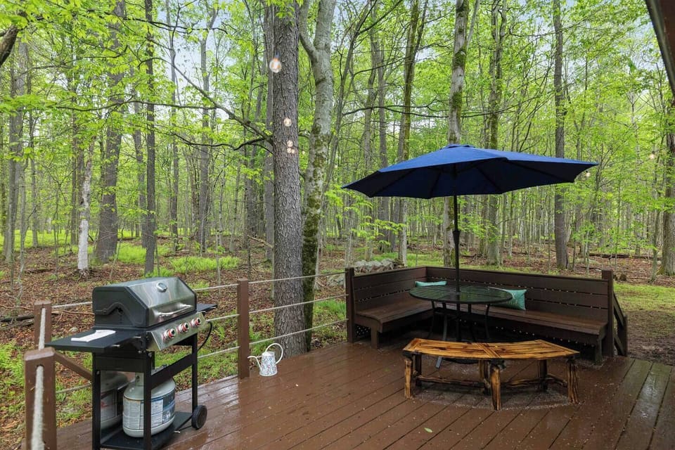 Cook, dine, and relax on this spacious outdoor deck featuring a gas grill, comfortable seating and a shaded umbrella set up overlooking peaceful wooded scenery. 