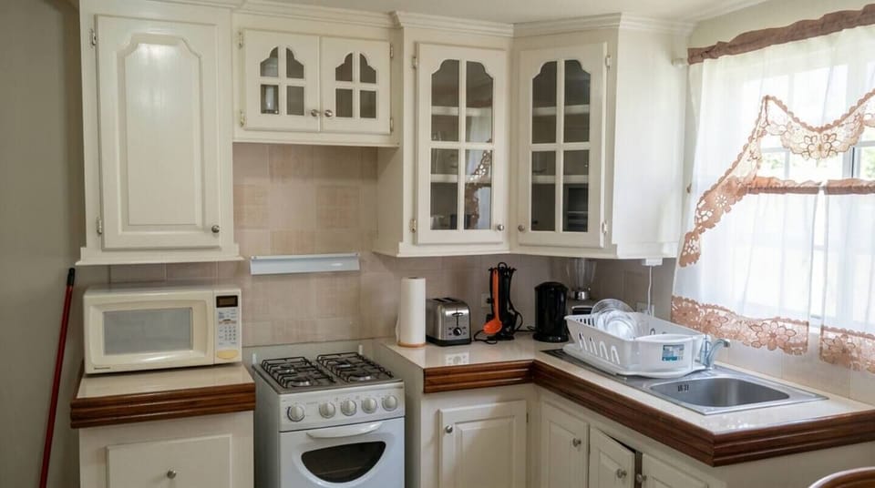 Cozy, fully equipped kitchen featuring classic white cabinetry, a gas stove, microwave, and toaster. Includes a convenient sink area, essential cookware, and bright natural light from the window—perfect for cooking homemade vacation meals.