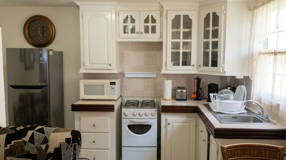 Charming, fully equipped kitchen featuring white cabinetry, a full-sized refrigerator, gas stove, microwave, and deep sink. Bright, cozy setup perfect for preparing home-cooked meals during your stay. Everything you need is right at hand!