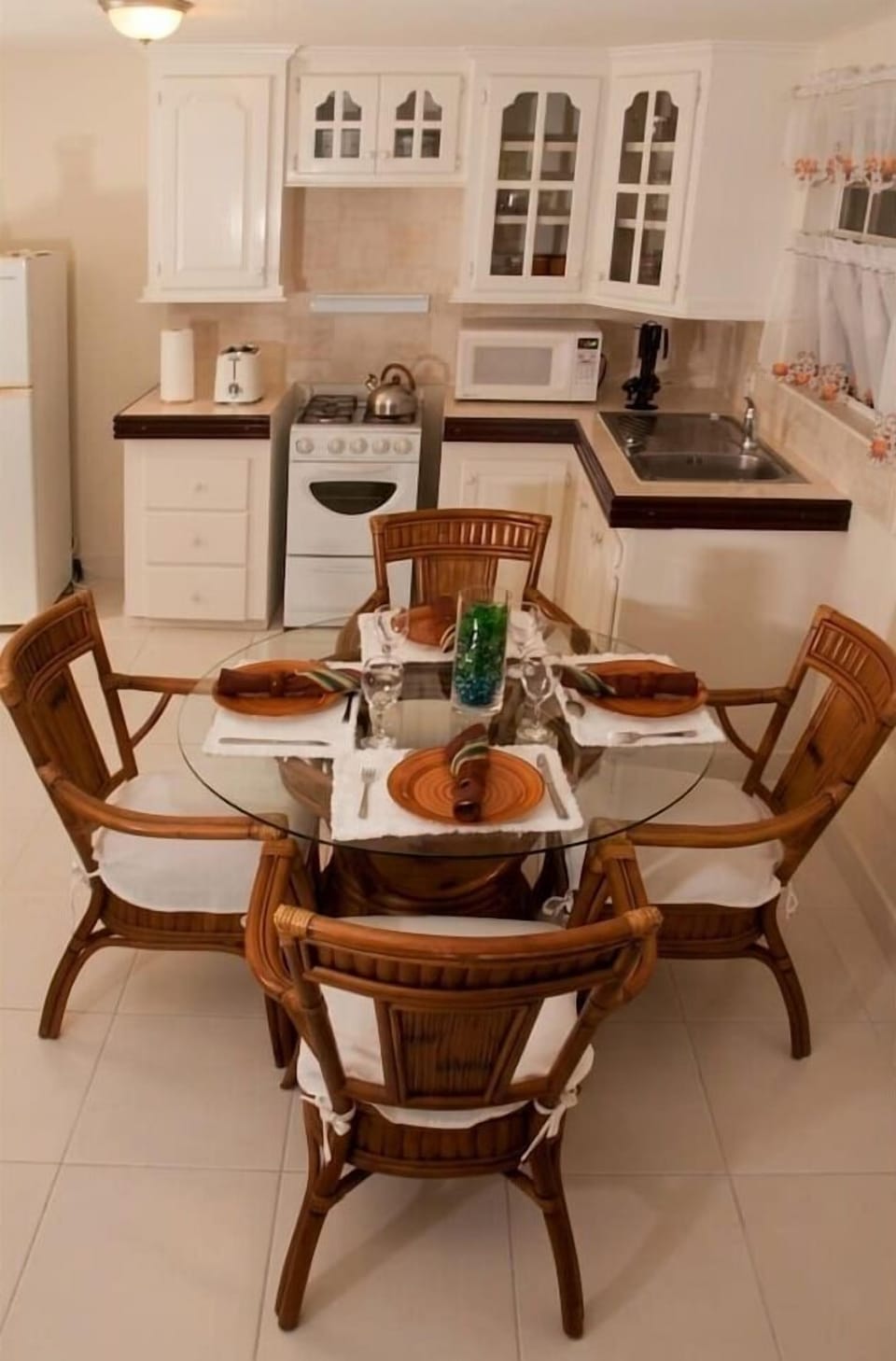 Cozy kitchen and dining area featuring a glass-top table with seating for four. Highlights include classic white cabinetry, fully equipped gas stove, microwave, refrigerator, and warm wooden accents perfect for home-cooked meals.