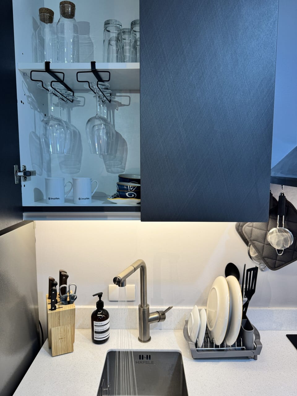 Sleek kitchenette with wine-glass rack, stocked basics, and LED lighting