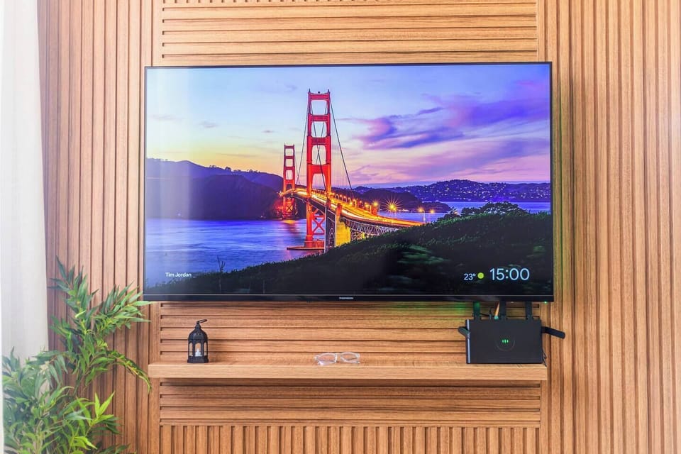 A sleek 55" 4K Smart TV blends into warm wood paneling, framed by soft decor and vibrant greenery. With high-speed fiber optic Wi-Fi, your favorite shows and apps are always just a click away.
