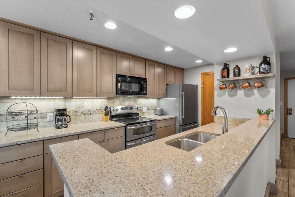 Step into your fully equipped kitchen with gleaming granite countertops, modern stainless appliances, and charming coffee mug display—everything you need to create delicious meals during your stay.