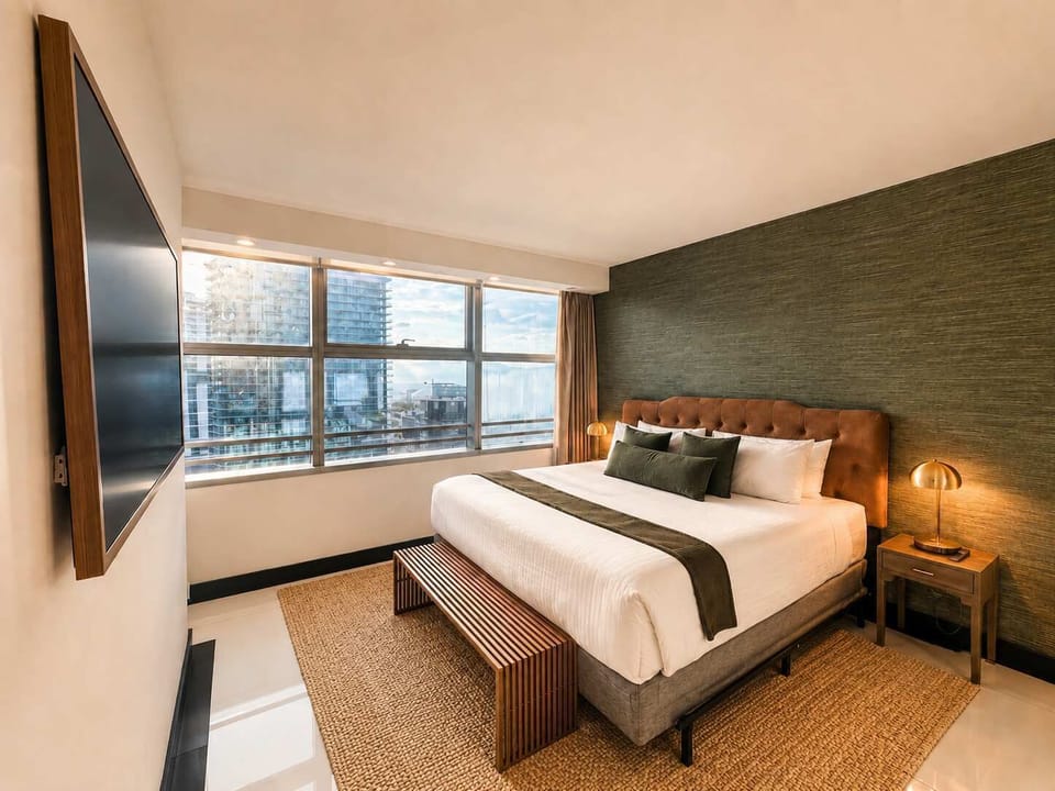 3404: Bedroom 1 (King) A chic city-view bedroom with a tufted leather headboard, layered linens, and warm brass accents.