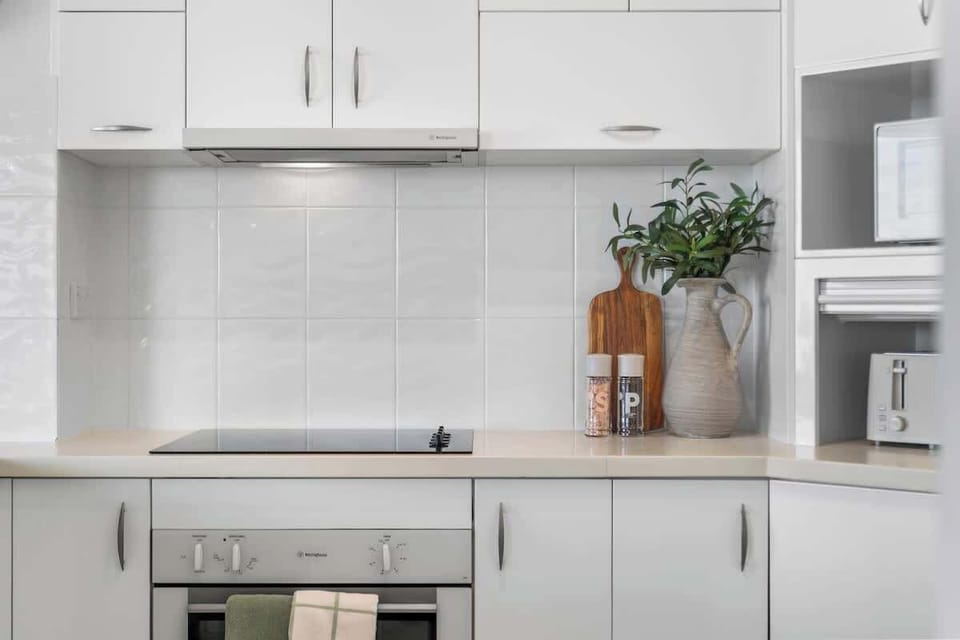 Cook with ease in this bright, contemporary kitchen featuring clean white cabinetry, a tiled splashback, a smooth cooktop, integrated oven, and thoughtful decorative accents.