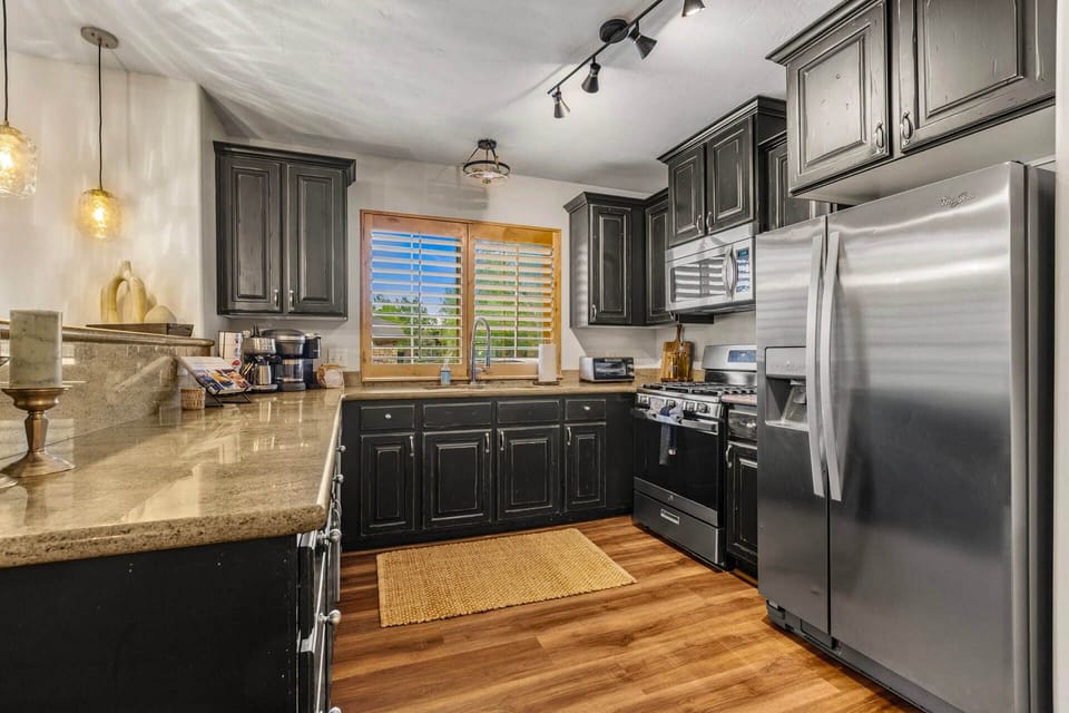 Your fully equipped kitchen features rich dark cabinetry, gleaming granite counters, and stainless steel appliances—perfect for preparing meals while enjoying natural light streaming through the plantation shutters.