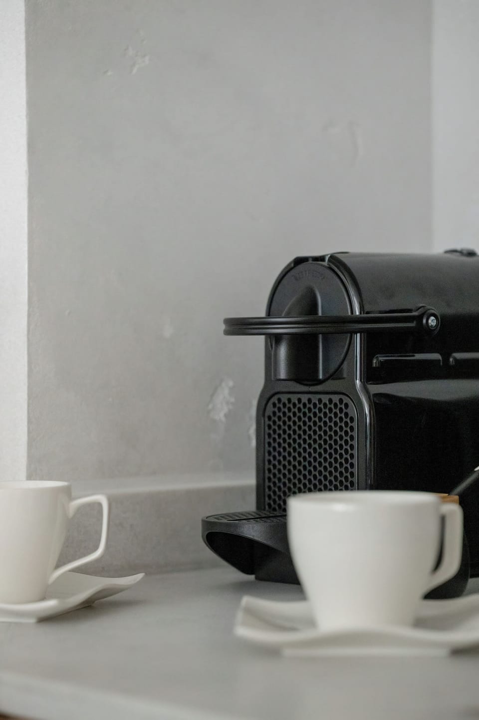A sleek black espresso capsule machine stands on the kitchen counter next to elegant white ceramic cups. This dedicated coffee corner promises a perfect start to every morning.