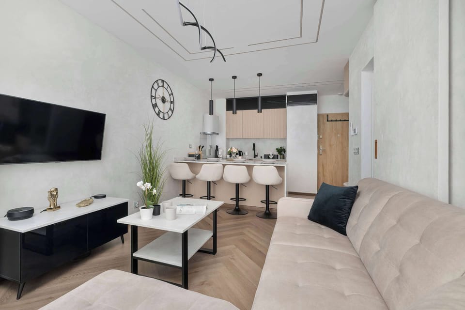 The open-plan living area smoothly transitions into the kitchen zone, showcasing a bright and airy layout. A white coffee table and dark media console contrast beautifully against the pale walls.
