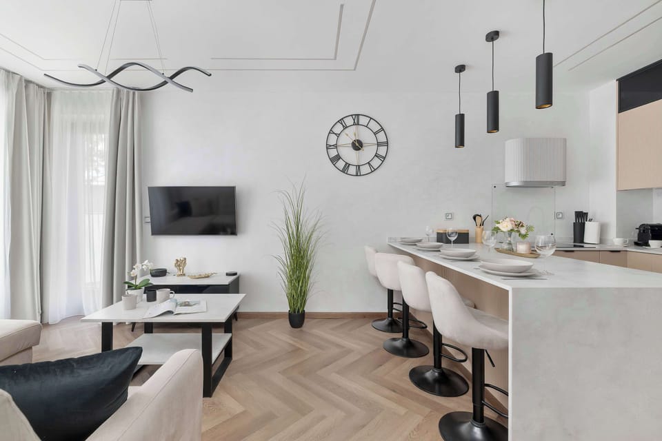 A view of the open-plan layout showcases a functional breakfast bar equipped with comfortable high stools. Sleek kitchen amenities and a wall clock add both style and convenience to the area.