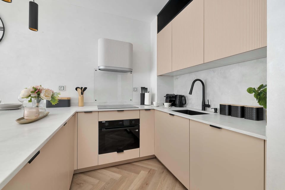 A focused view of the kitchenette reveals a built-in modern oven and a clean induction cooktop. The pastel-toned upper cabinets provide ample storage while maintaining a bright aesthetic.
