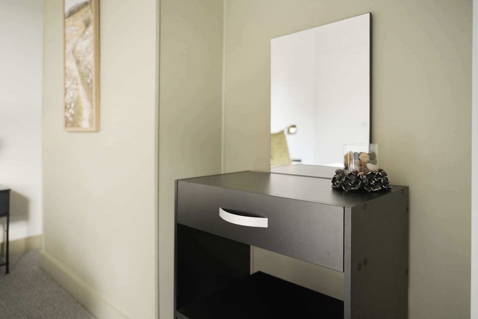 The first double bedroom combines comfort and practicality with a double bed, TV, dresser, two bedside tables, and storage. Its cupboard contains the boiler, clothes dryer, ironing board, iron, and vacuum.