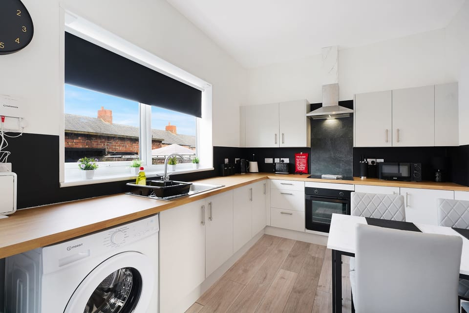 Featuring a four-seater dining table, the kitchen is equipped with a fridge freezer, oven, hob, microwave, washing machine, and essential kitchenware. Tea, coffee, sugar, and a first aid kit are provided.