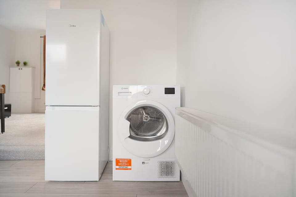 The kitchen is well equipped with a four-seater dining table, fridge freezer, oven, hob, microwave, washing machine, and essential kitchenware. A door from the kitchen provides direct access to the backyard.