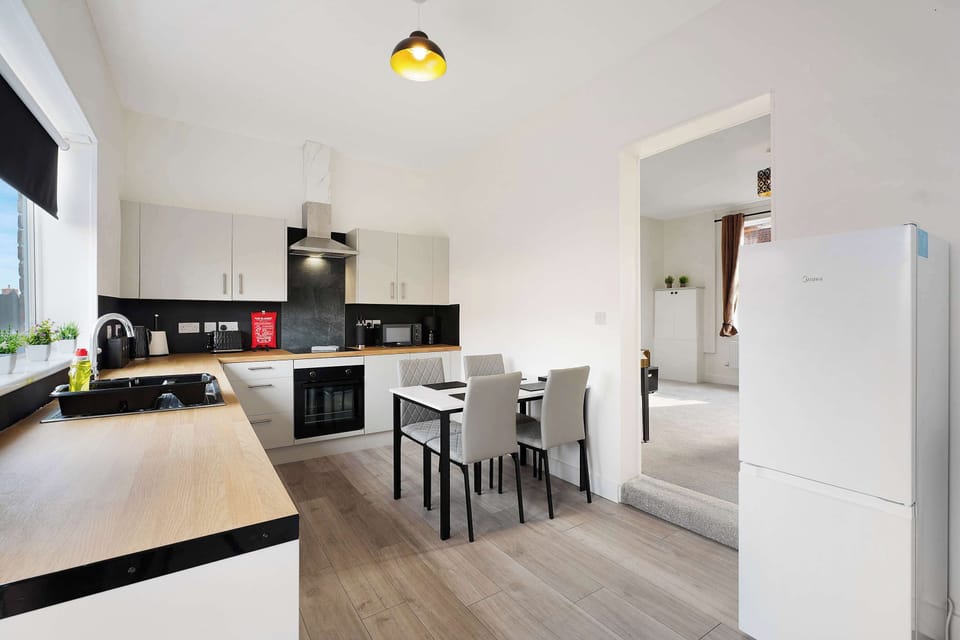 The kitchen includes a four-seater dining table, fridge freezer, washing machine, oven, hob, microwave, and sink. Kitchenware, tea, coffee, sugar, and a first aid kit are provided, with access to the backyard.