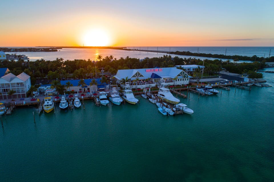 A breathtaking sunset casts golden light over the marina, where sleek boats rest on turquoise waters and the evening sky glows with tropical serenity.