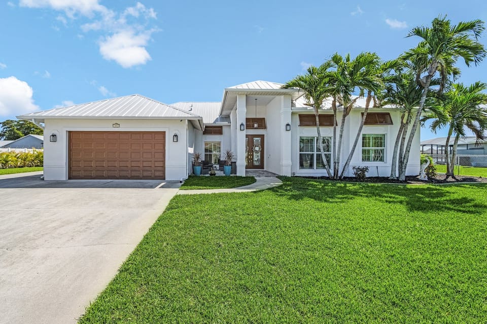Striking curb appeal featuring a manicured green lawn, tropical palm trees, and full impact-resistant windows and doors.