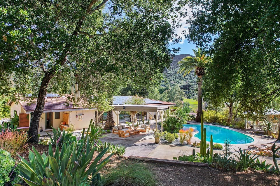 Lush hillside retreat with a sparkling pool, covered lounge area, and mountain views.