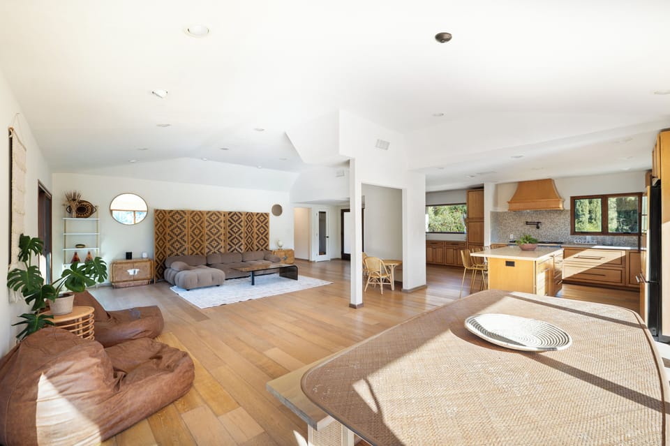 Open-concept living, dining, and kitchen area with warm wood floors, relaxed seating, and mountain-view windows.