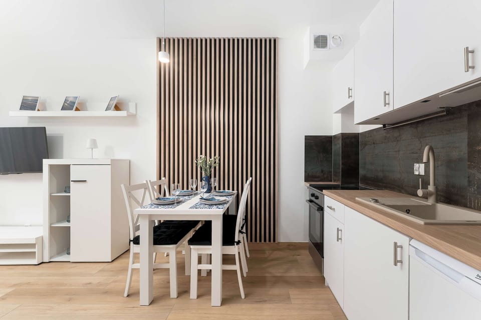 The open-concept design connects a small dining table directly to a linear white kitchenette. A tall white media cabinet sits against the opposite wall.