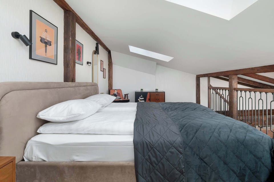 The loft bedroom is captured from another angle, highlighting the wooden safety railing that overlooks the lower floor. The bed is neatly made, and a skylight brings natural light into the sloped space.