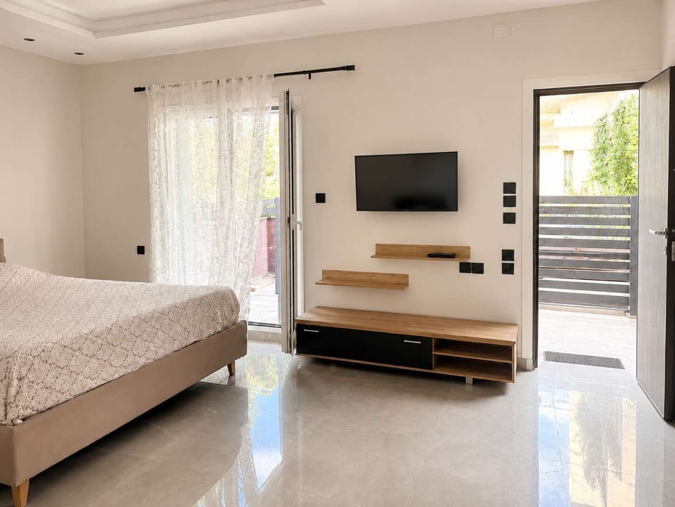 A bright bedroom and lounge space with a cozy bed, wall-mounted TV, patio doors, and plenty of natural light. The room feels calm, practical, and comfortable for everyday living