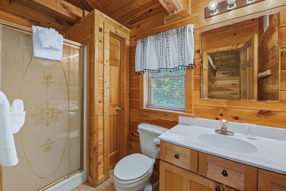 This cozy cabin bathroom brings rustic comfort to your mountain retreat with warm wood walls and thoughtful touches like fresh towels and natural light.