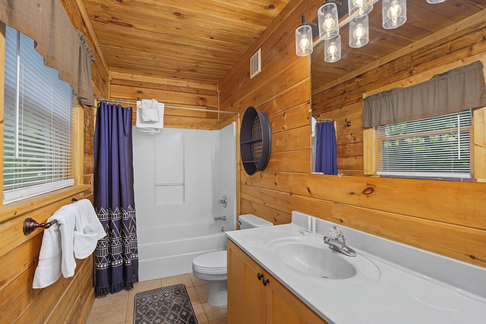 Freshen up in this warm cabin-style bathroom with fluffy towels, a full tub-shower combo, and rustic wood details that make every stay feel like a peaceful retreat.